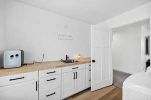 Bar featuring butcher block counters, white cabinets, light wood finished floors, and washer and dryer