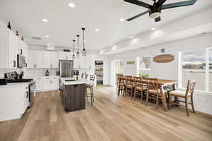 Kitchen featuring two tone cabinets, stainless steel appliances, a kitchen bar, a center island with sink, and decorative backsplash