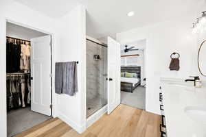 Full bathroom featuring double vanity, ensuite bath, a shower stall, a walk in closet, and light wood-style floors
