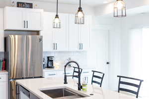 Kitchen featuring freestanding refrigerator, white cabinets, decorative light fixtures, light stone countertops, and tasteful backsplash