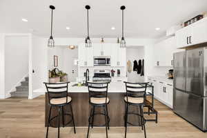 Kitchen featuring stainless steel appliances, an island with sink, a breakfast bar, light wood-style floors, and dual tone cabinetry
