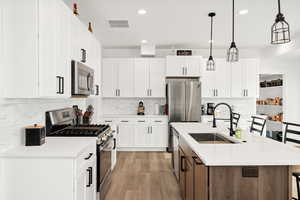 Dual tone kitchen featuring a kitchen bar, stainless steel appliances, two tone cabinetry, an island with sink, and light wood-type flooring