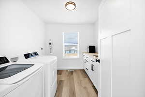 Laundry room with light wood-style flooring, cabinet space, and washing machine and dryer