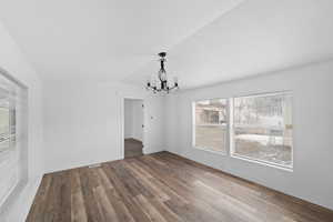 Unfurnished dining area featuring lofted ceiling, hanging lights, and wood finished floors