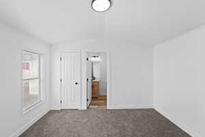 Unfurnished bedroom featuring dark carpet, vaulted ceiling, ensuite bathroom, and a closet