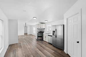 Kitchen featuring stainless steel appliances, white cabinetry, suspended lighting, light countertops, and dark wood finished floors