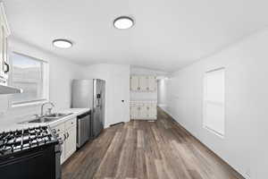 Kitchen with light countertops, dark wood-type flooring, stainless steel appliances, vaulted ceiling, and ornamental molding
