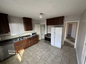Kitchen featuring stainless steel appliances, light tile patterned flooring, decorative backsplash, and dark wood finish cabinetry