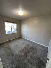Unfurnished room featuring dark colored carpet and baseboards