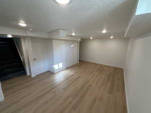 Finished basement with a textured ceiling and light wood-type flooring