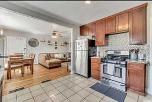 Kitchen with stainless steel appliances, open floor plan, light tile patterned floors, a ceiling fan, and light stone counters