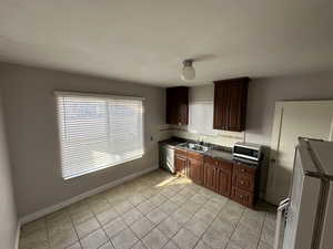Kitchen with stainless steel appliances, light tile patterned flooring, decorative backsplash, and dark wood finish cabinets