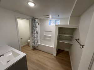 Bathroom featuring double vanity, a textured ceiling, light wood finished floors, shower / bath combo with shower curtain, and a closet