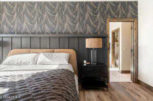 Bedroom with wallpapered walls, wood finished floors, and an accent wall