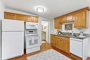 Kitchen with white appliances, dark wood finished floors, dark stone countertops, and wood finish cabinetry