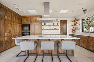 Kitchen featuring wood finish cabinetry, island range hood, a center island, black appliances, and a breakfast bar