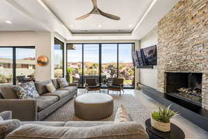 Living room featuring a fireplace, ceiling fan, a tray ceiling, and recessed lighting