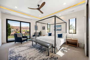 Bedroom with light colored carpet, ceiling fan, a tray ceiling, multiple windows, and access to exterior