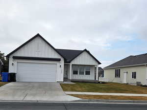 View of front facade with board and batten siding, driveway, a front lawn, and an attached garage