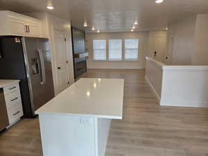 Kitchen featuring open floor plan, stainless steel appliances, white cabinets, light wood-type flooring, and a center island