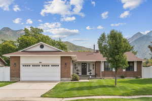 Ranch-style house with a mountain view, an attached garage, concrete driveway, brick siding, and roof with shingles
