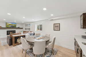 Dining room with wainscoting, light wood-style flooring, a brick fireplace, brick wall, and recessed lighting