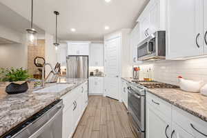 Kitchen featuring stainless steel appliances, light stone countertops, wood tiled floors, white cabinetry, and backsplash