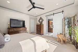 Bedroom with a barn door, light colored carpet, ceiling fan, ensuite bathroom, and recessed lighting