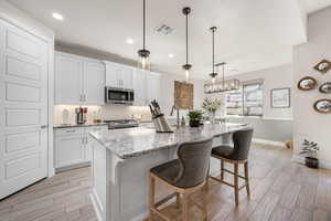 Kitchen with white cabinets, a kitchen bar, wood finish floors, and backsplash