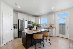 Kitchen with light stone countertops, a kitchen bar, stainless steel appliances, a center island, and light wood-type flooring