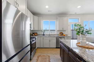 Kitchen featuring stainless steel appliances, light wood-style floors, two tone color scheme, light stone countertops, and recessed lighting