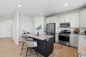 Kitchen with stainless steel appliances, a kitchen breakfast bar, light wood-type flooring, light stone countertops, and a center island