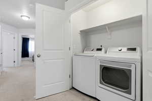Laundry area with light colored carpet and washer and clothes dryer