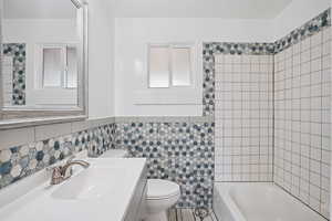 Updated bathroom with tile walls, vanity, a wainscoted wall, and shower / washtub combination