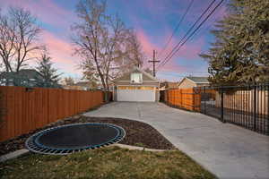 Fenced backyard featuring a trampoline, a garage, and an outdoor structure