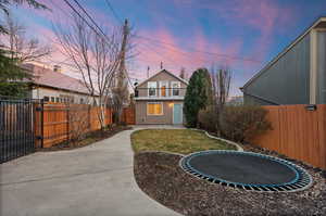 Back of house at dusk with a fenced backyard, a trampoline, a gate, and a patio