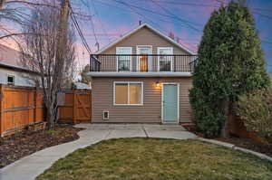 Back of property at dusk featuring a fenced backyard, a patio, a gate, and a balcony