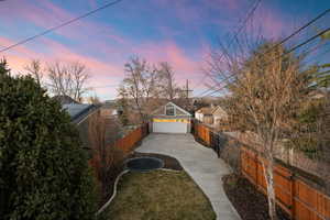 Yard at dusk featuring a fenced backyard, a trampoline, a garage, and driveway