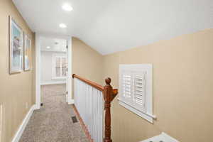 Hall with carpet flooring, an upstairs landing, vaulted ceiling, and recessed lighting