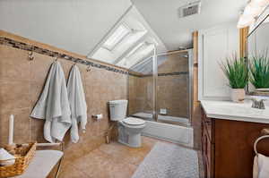 Full bathroom with vanity, enclosed tub / shower combo, tile walls, a skylight, and light tile patterned floors