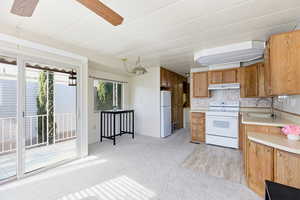 Kitchen with white appliances, light countertops, wood finish cabinets, light colored carpet, and pendant lighting