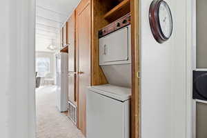 Laundry area with light colored carpet and stacked washer / drying machine