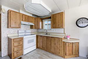 Kitchen with white range with electric cooktop, light countertops, and wood finish cabinets
