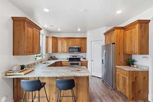 Kitchen with stainless steel appliances, a peninsula, wood finish cabinetry, a breakfast bar, and dark wood finished floors