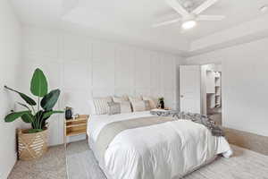 Primary Bedroom with light colored carpet, a raised ceiling, a ceiling fan, a decorative wall, and a spacious closet