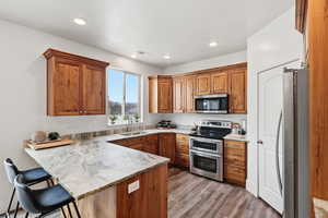 Kitchen with a peninsula, stainless steel appliances, a kitchen breakfast bar, wood finish cabinets, and light stone counters