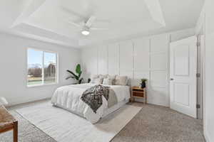 Primary Bedroom with a raised ceiling, light carpet, and a ceiling fan