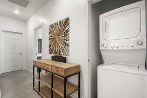 Laundry area featuring stacked washer and clothes dryer and light carpet