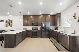 Kitchen with dark wood finish cabinetry, a peninsula, a kitchen breakfast bar, stainless steel appliances, and pendant lighting