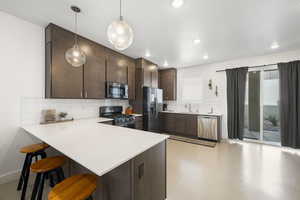 Kitchen with dark wood finish cabinets, a breakfast bar, a peninsula, stainless steel appliances, and hanging light fixtures